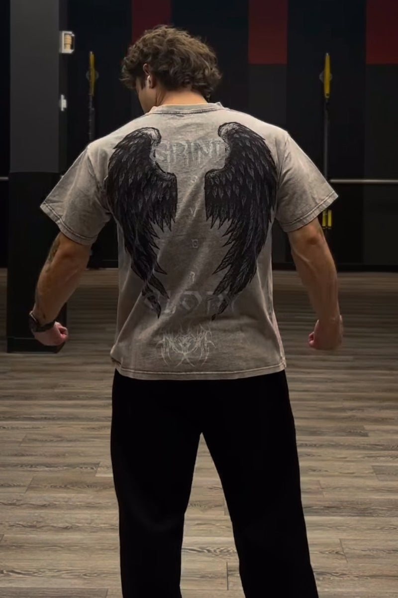 Person wearing a gray t-shirt with black wings and text design, standing in an indoor setting.